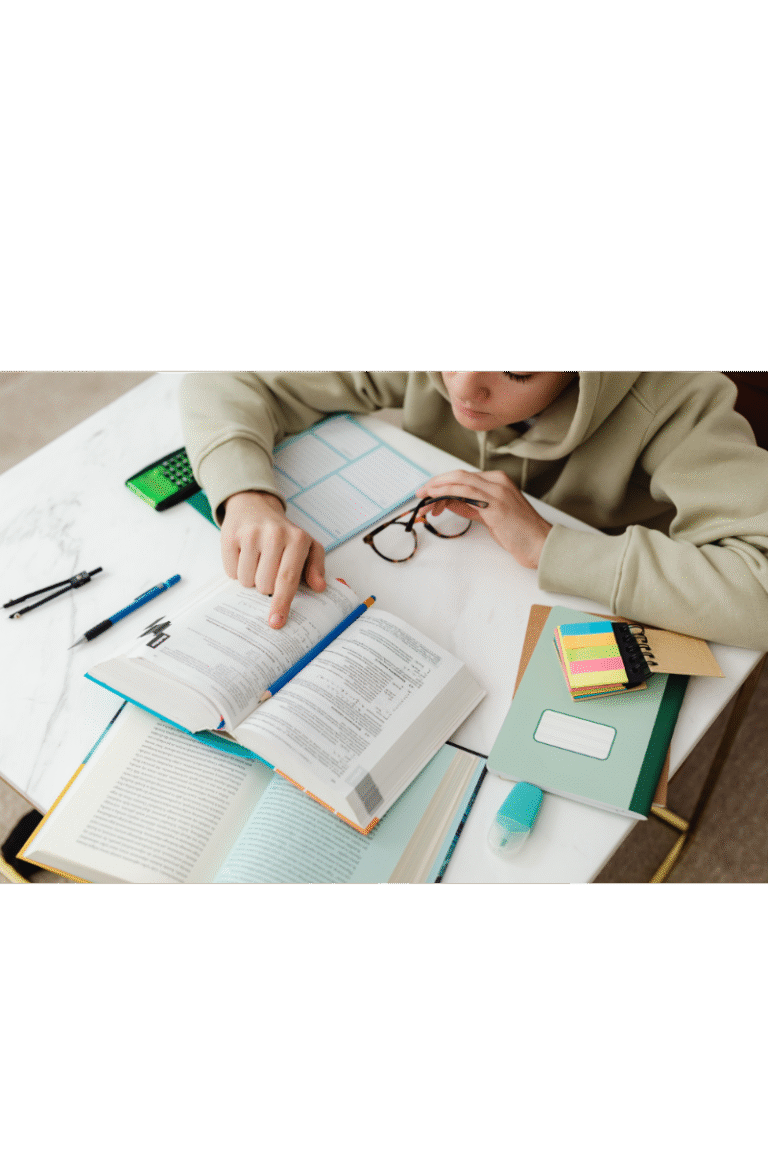 A person at a desk reading a book with a pair of glasses in front of them