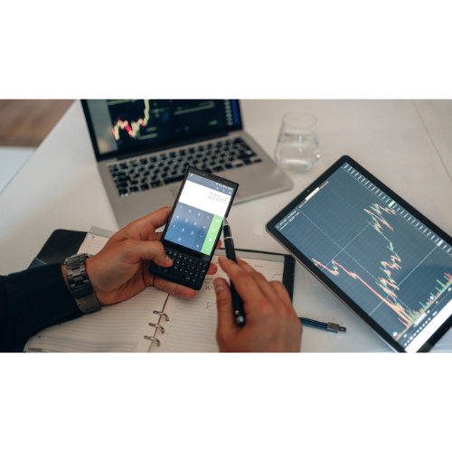 Man holding a mobile phone with a laptop open and a tablet screen showing